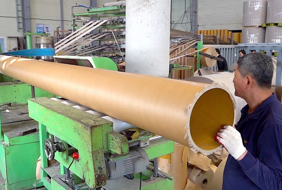 Worker inspecting a large paper core in a paper mill